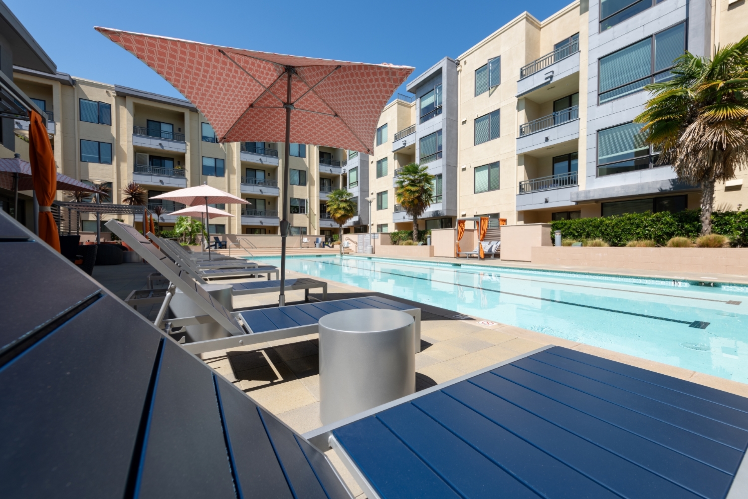 Apartments in Foster City-One Hundred Grand Swimming Pool Surrounded by Shaded Seating and Lounge Chairs